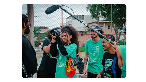 Grupo de jovens filmando um documentário na favela, com câmera e microfone, promovendo a cultura local e a inclusão.