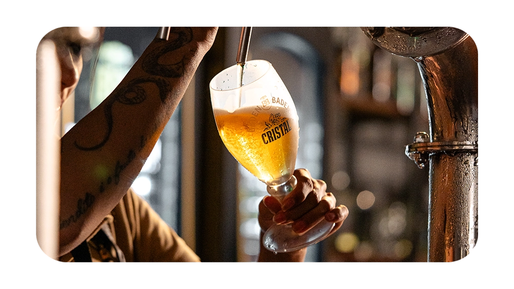 Cerveja Cristal sendo servida em copo, destacando o talento do barman e a atmosfera acolhedora do bar. Aprecie com moderação.