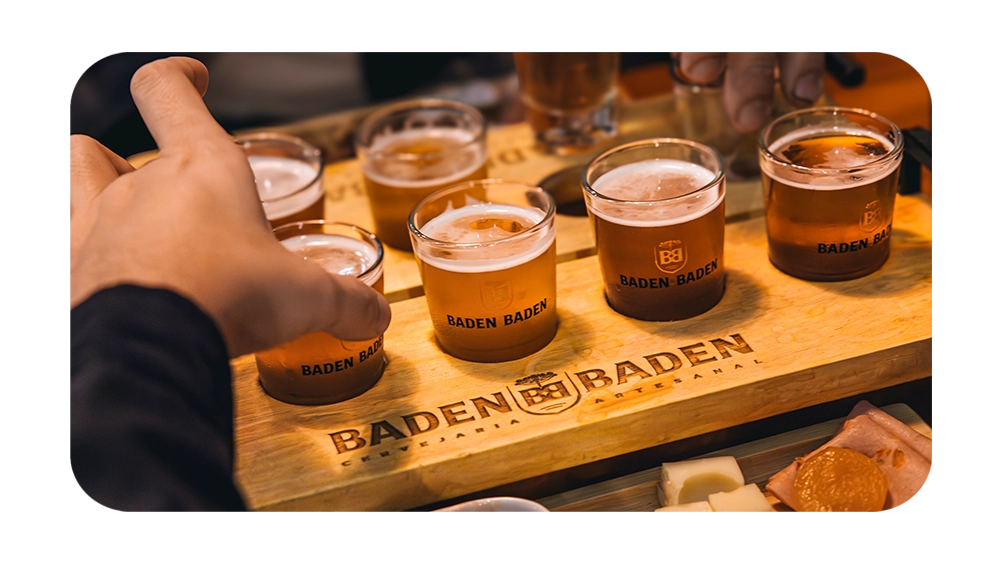 Degustação de cervejas artesanais Baden Baden em tábuas de madeira, com copos cheios e acompanhamentos variados. Atmosfera descontraída e saborosa.