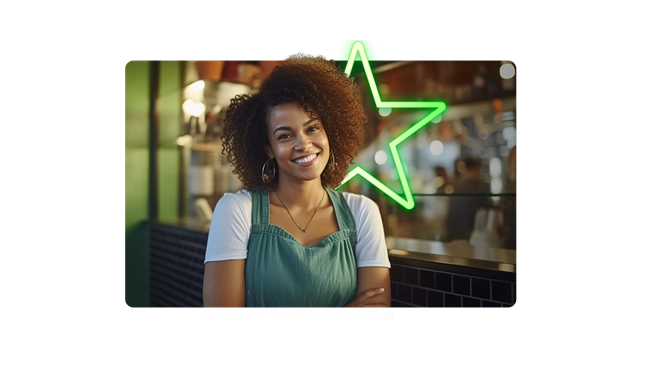 Mulher sorridente em ambiente moderno, com cabelo cacheado e moletom verde, ao fundo, uma luminária em formato de estrela iluminada.